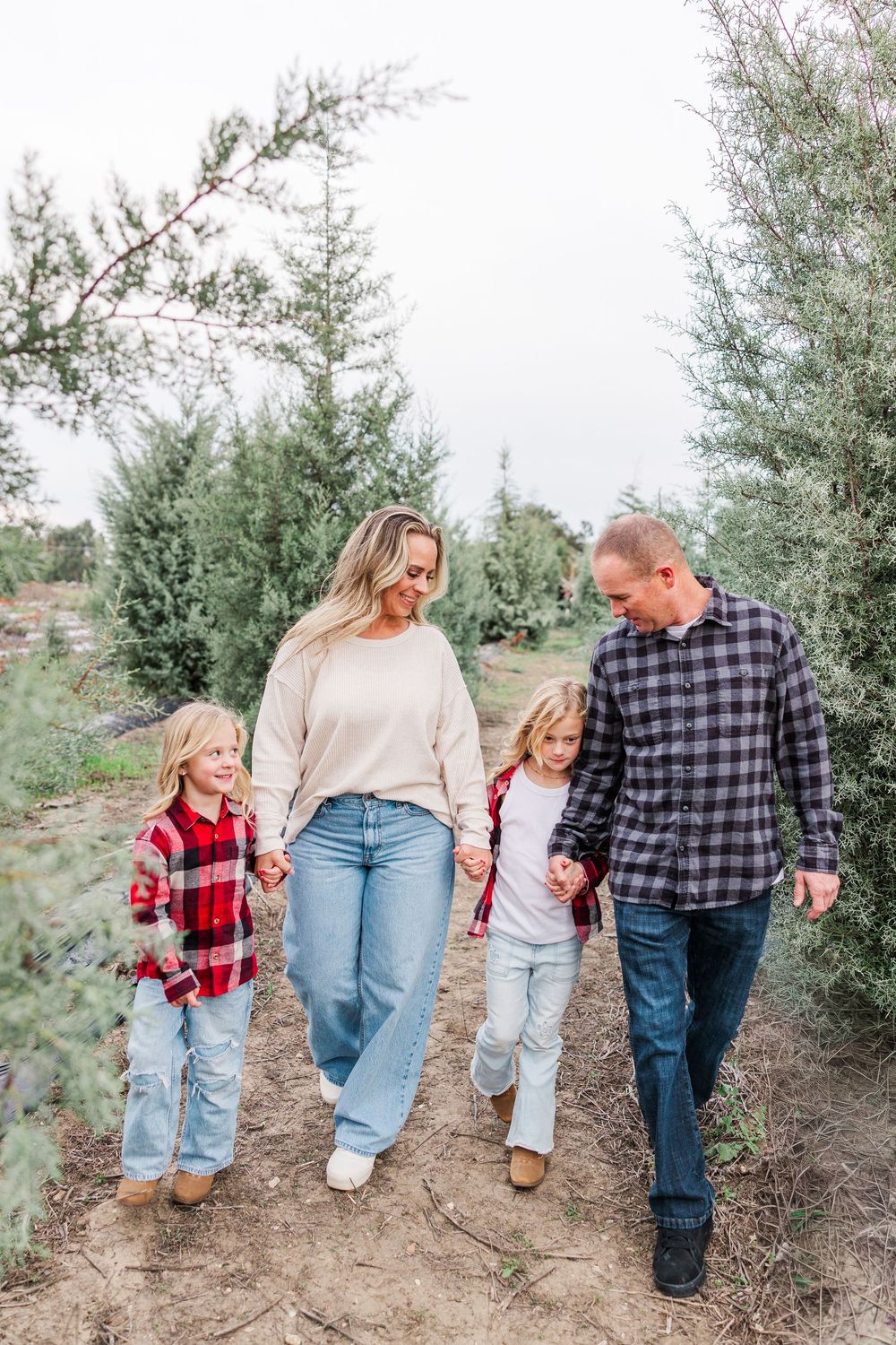 Family walking together through evergreen trees wearing coordinated casual outfits in matching neutral tones.