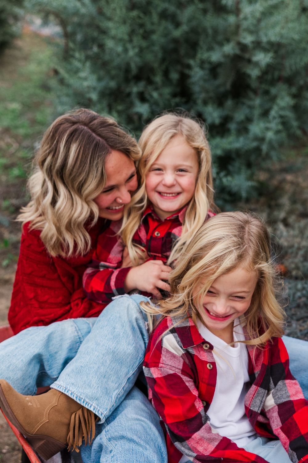 A family wearing coordinated red and plaid outfits sits together outdoors sharing joyful laughter in a casual portrait setting.