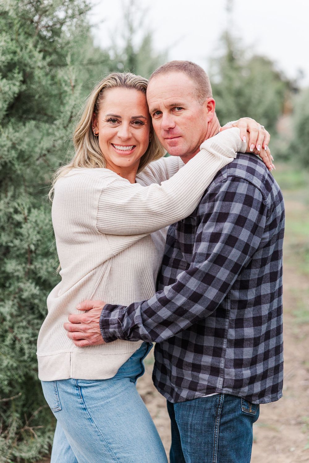 A couple in casual attire shares intimate embraces while posing together in an outdoor setting with trees in the background.