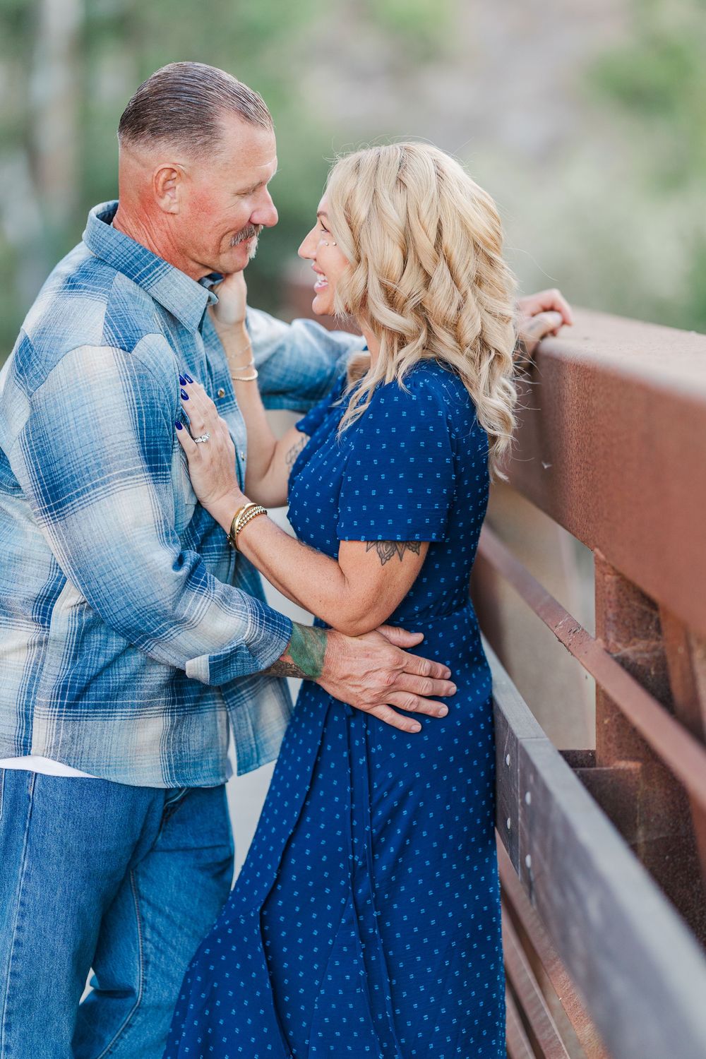 A romantic couple in coordinating blue outfits share tender moments along a wooden railing outdoors.