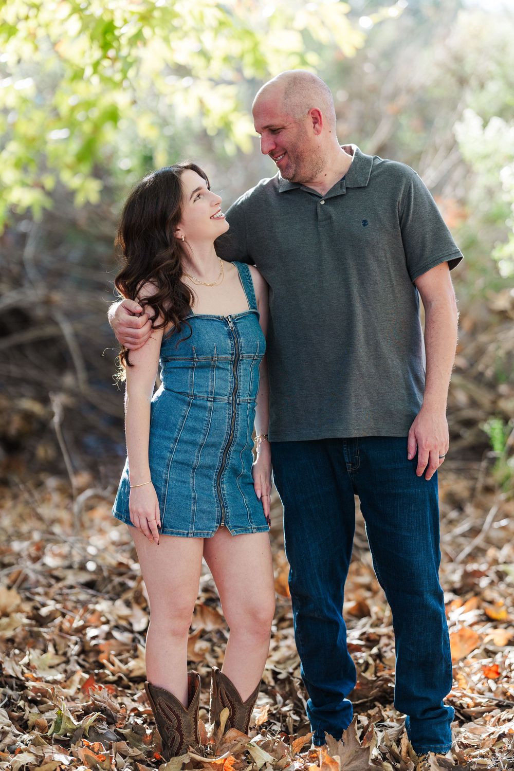 A couple shares romantic moments together while standing among fallen autumn leaves in a wooded setting.