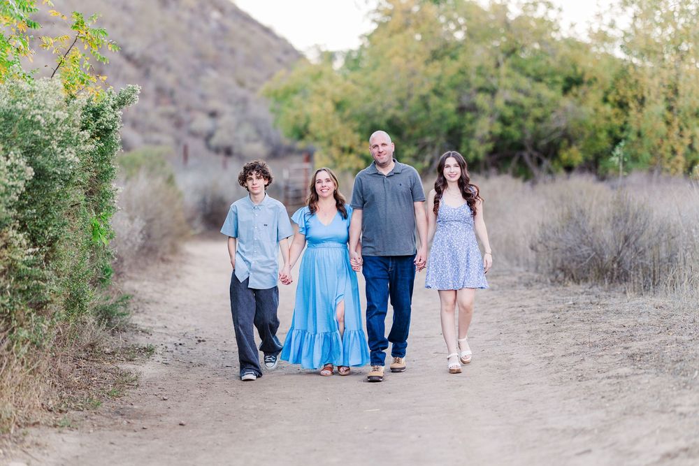 A group in coordinated blue and white outfits walks together on a dirt path surrounded by desert brush and mountains.