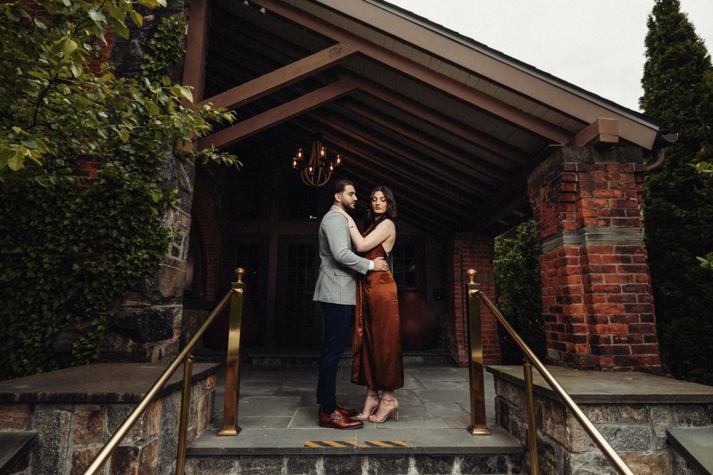 Wedding couple embracing on rustic wooden porch with brick building backdrop.