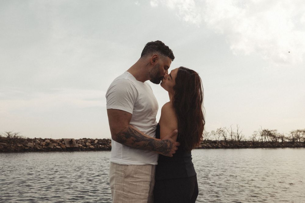 Romantic couple embraces near a waterfront at sunset creating silhouettes against the ocean backdrop.