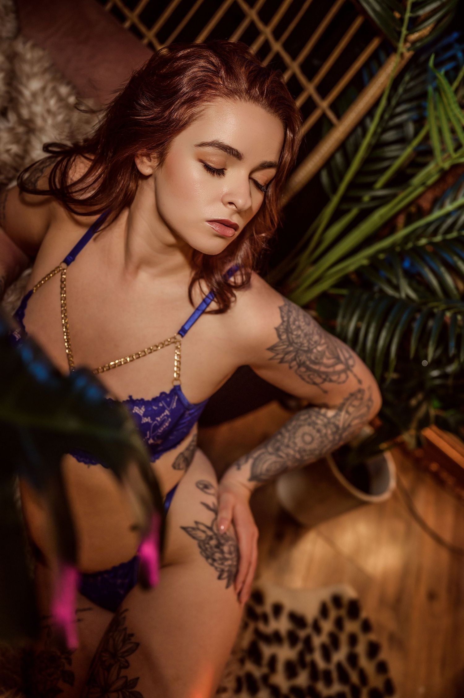 A model in purple lingerie poses against a backdrop of tropical palm leaves and warm lighting.