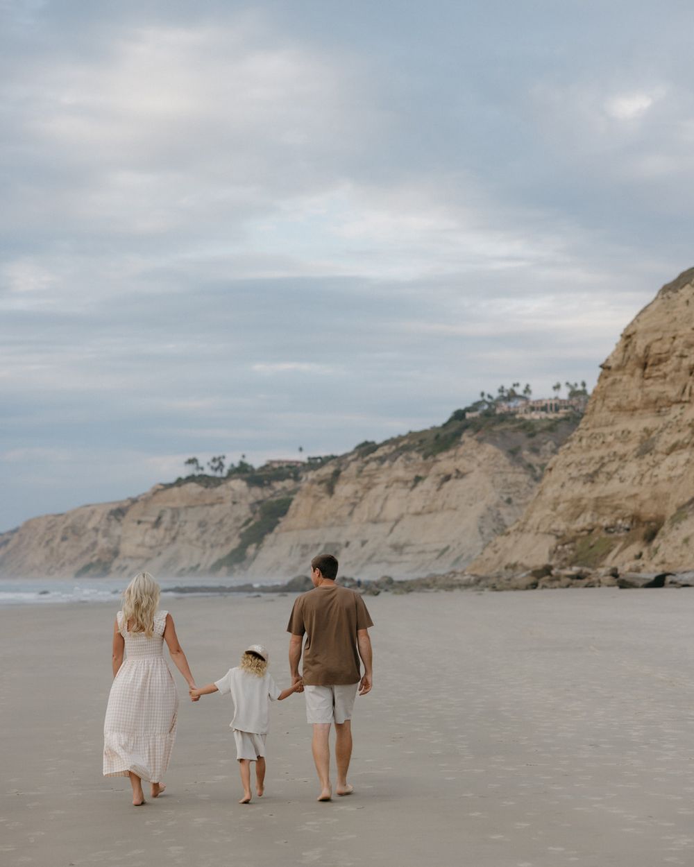 Family walking together on a scenic beach with tall cliffs in the background on an overcast day.