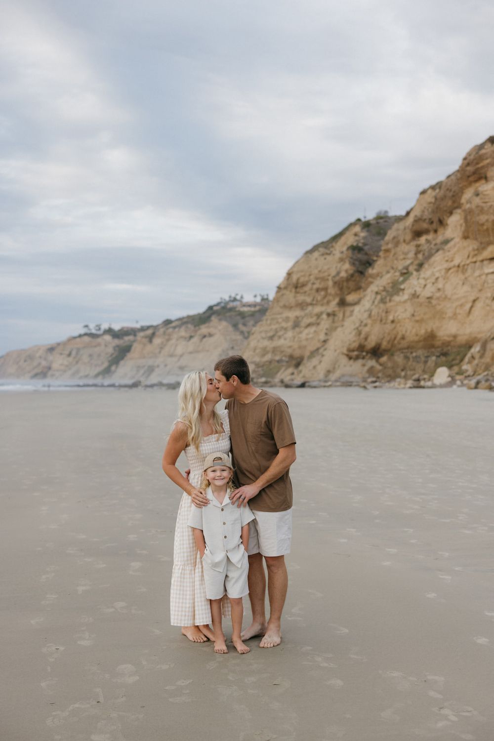 Family enjoying a tender moment together while walking on a scenic beach with cliffs in the background.