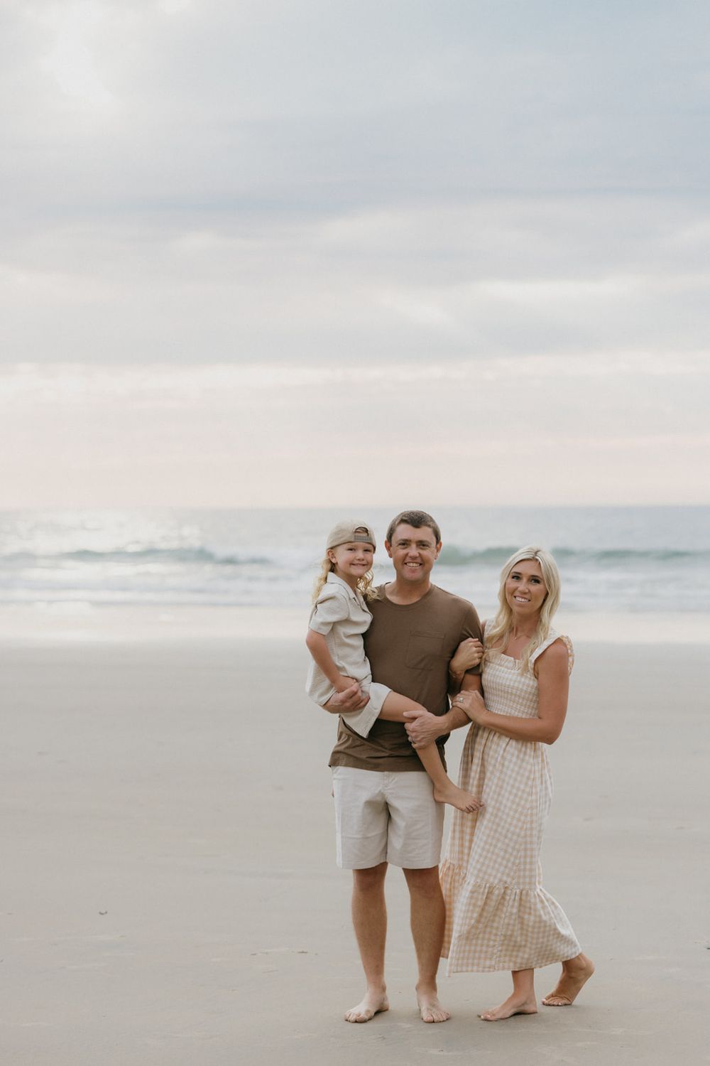 Family in coordinated neutral outfits sharing tender moments on a misty beach.