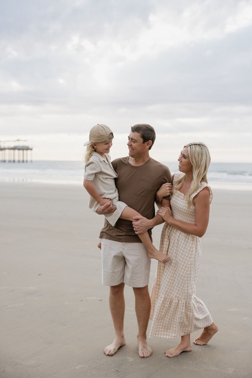 Family in casual beachwear poses together on overcast day by the ocean.