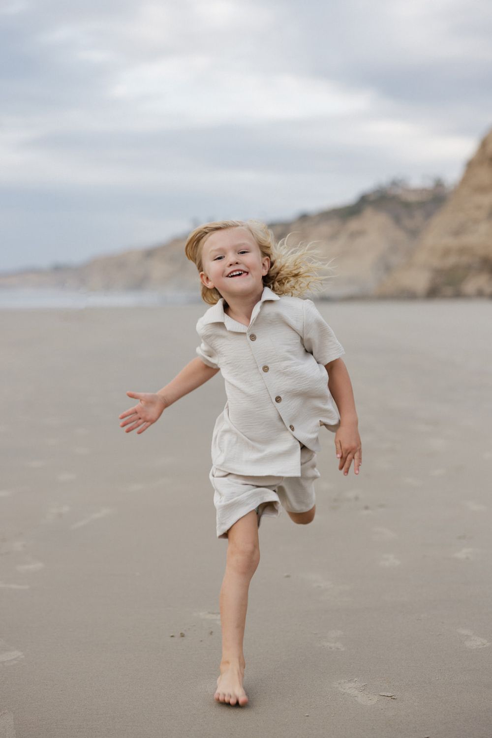 Young child in white clothing plays joyfully on a sandy beach.
