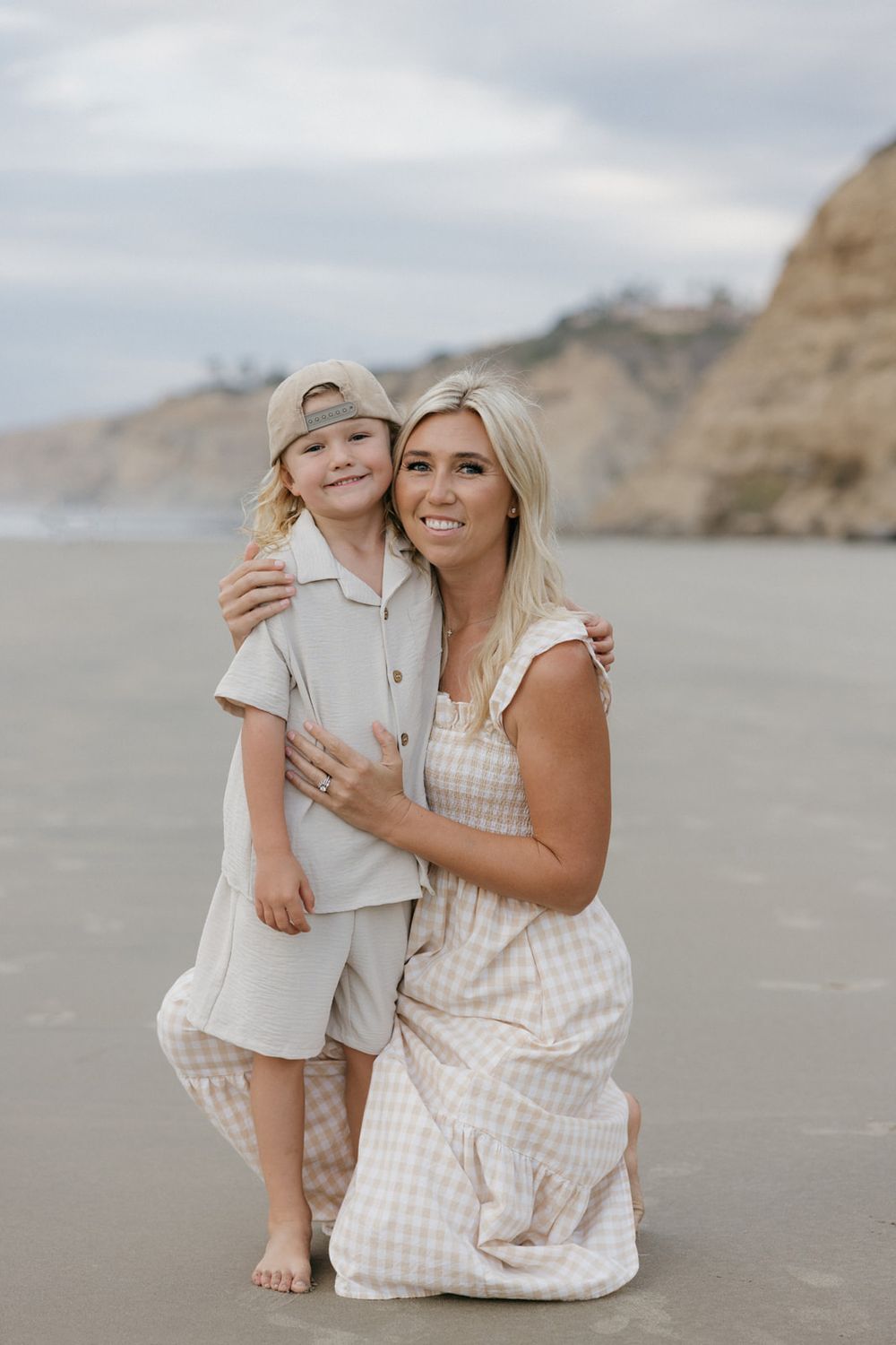Mother and child share affectionate moments while sitting on a beach.