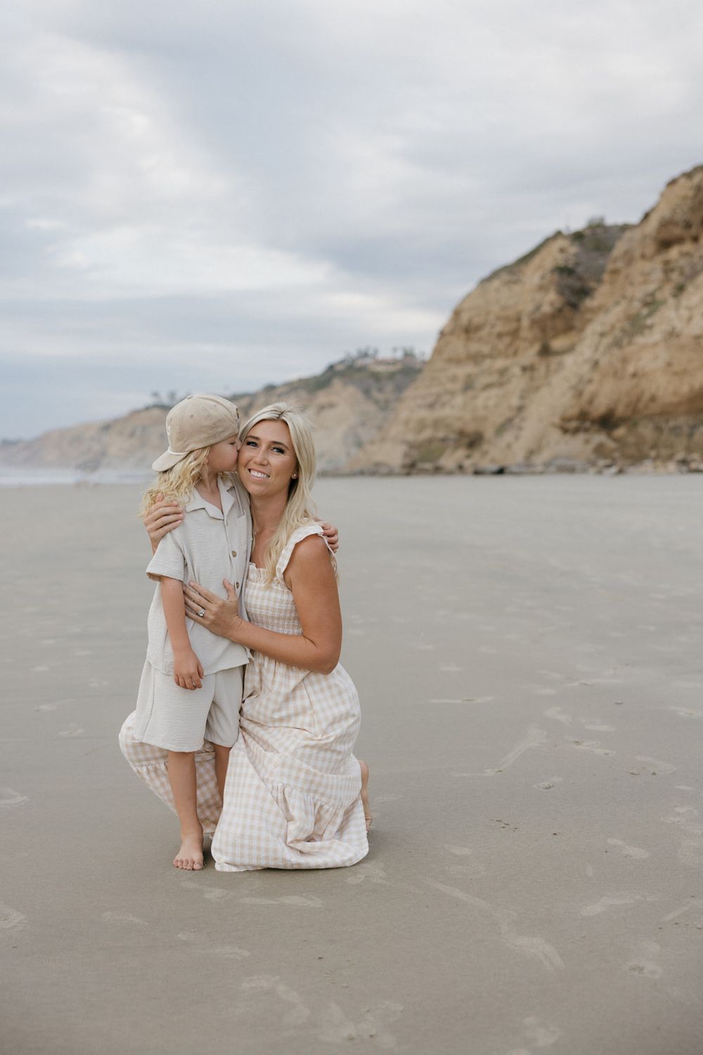 Mother and child sharing sweet moments together on a sandy beach with coastal cliffs.