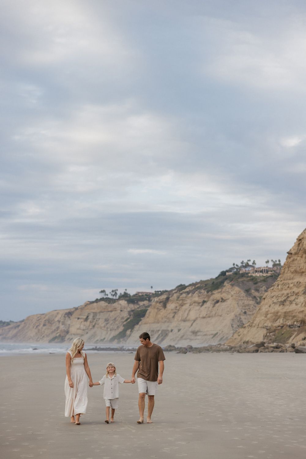 Family walking together on a cloudy beach with coastal cliffs in the background at La Jolla Shores, California.