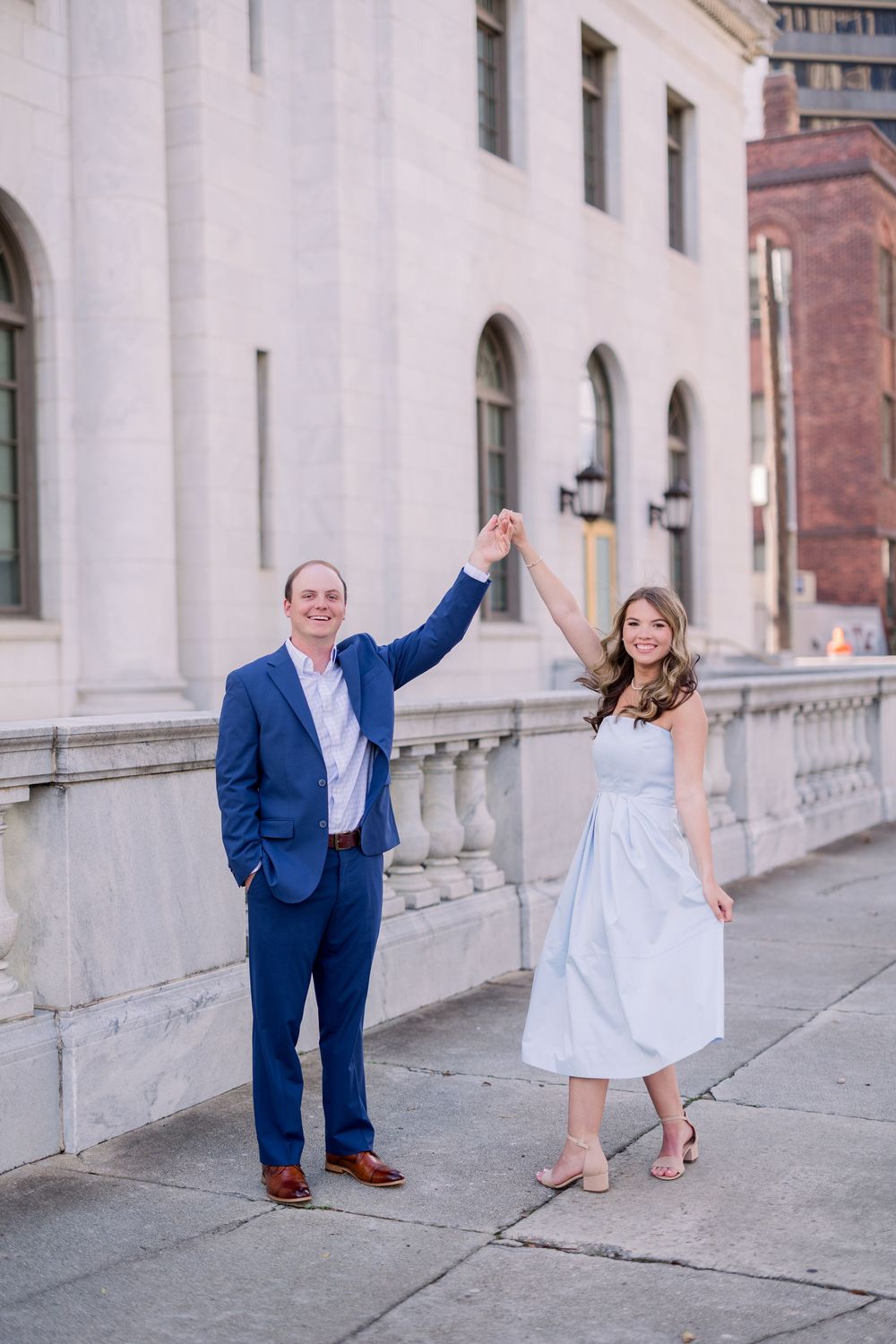 A couple holding hands up in celebration in front of a classic white building.