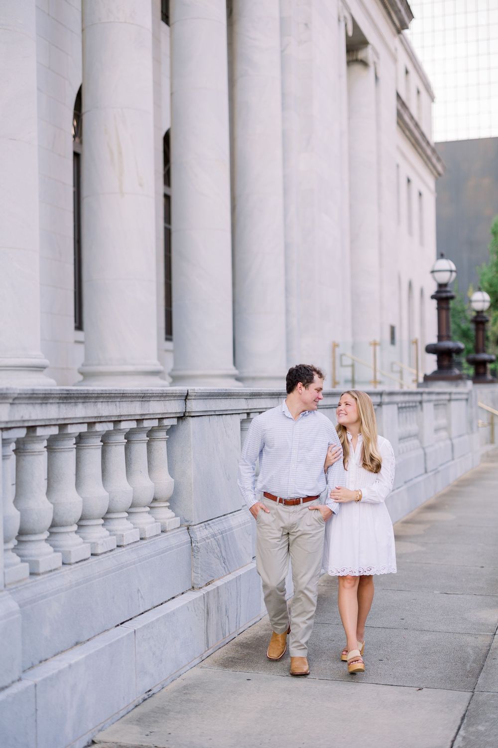 Two people in white and khaki outfits dance along a columned walkway.
