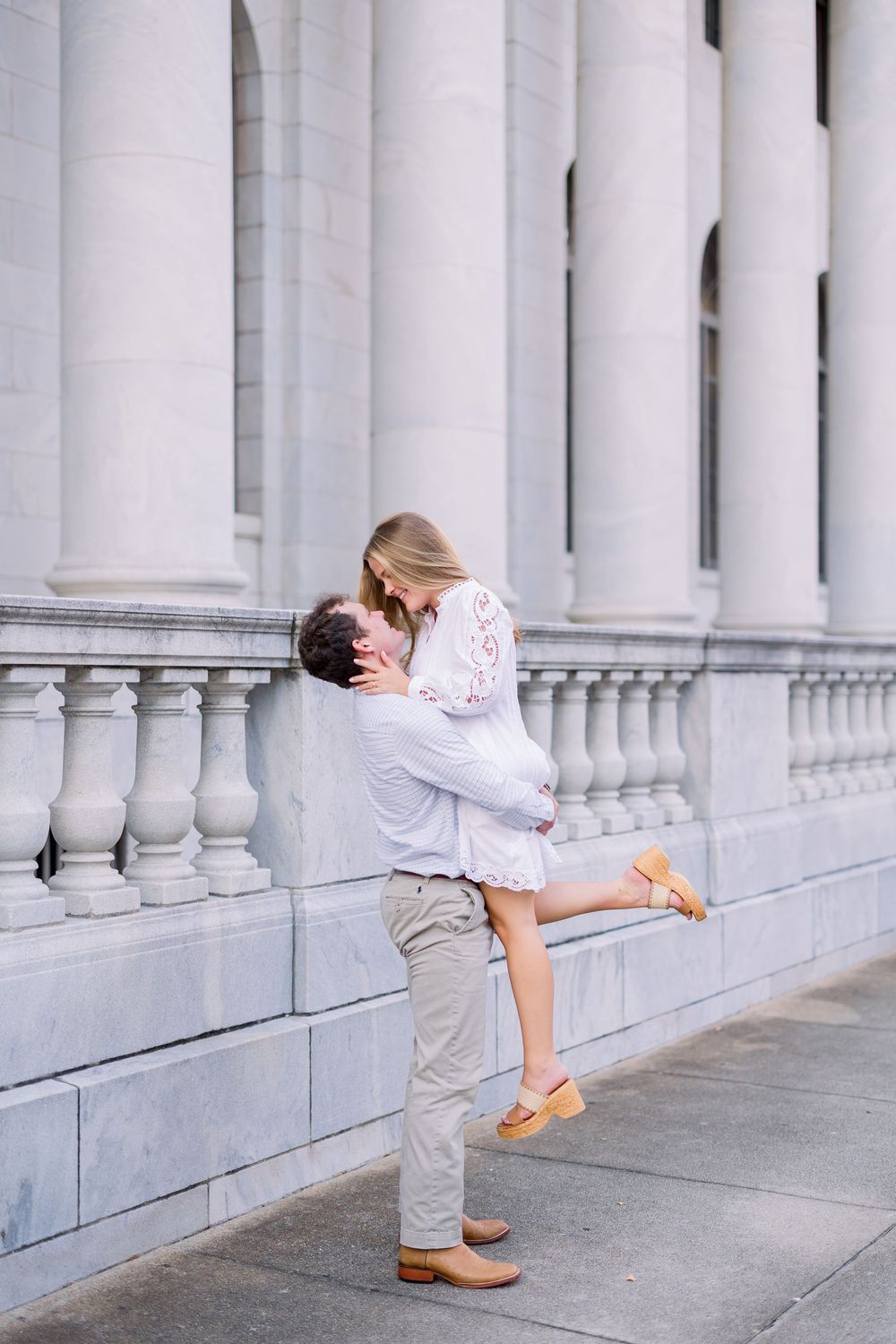 A romantic couple embracing in front of white stone columns with the woman lifted off her feet.