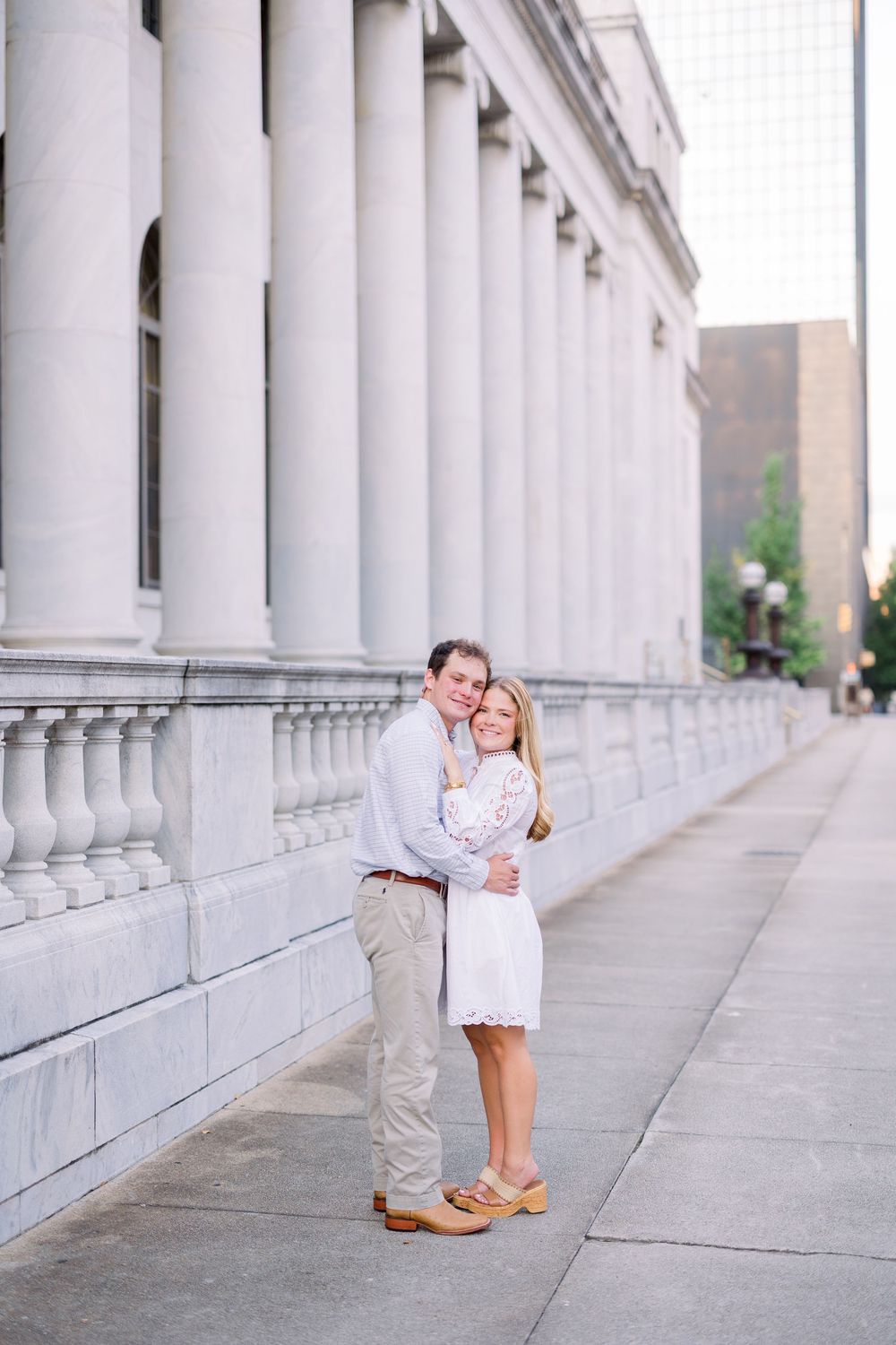 A couple standing close together against a backdrop of white architectural columns.