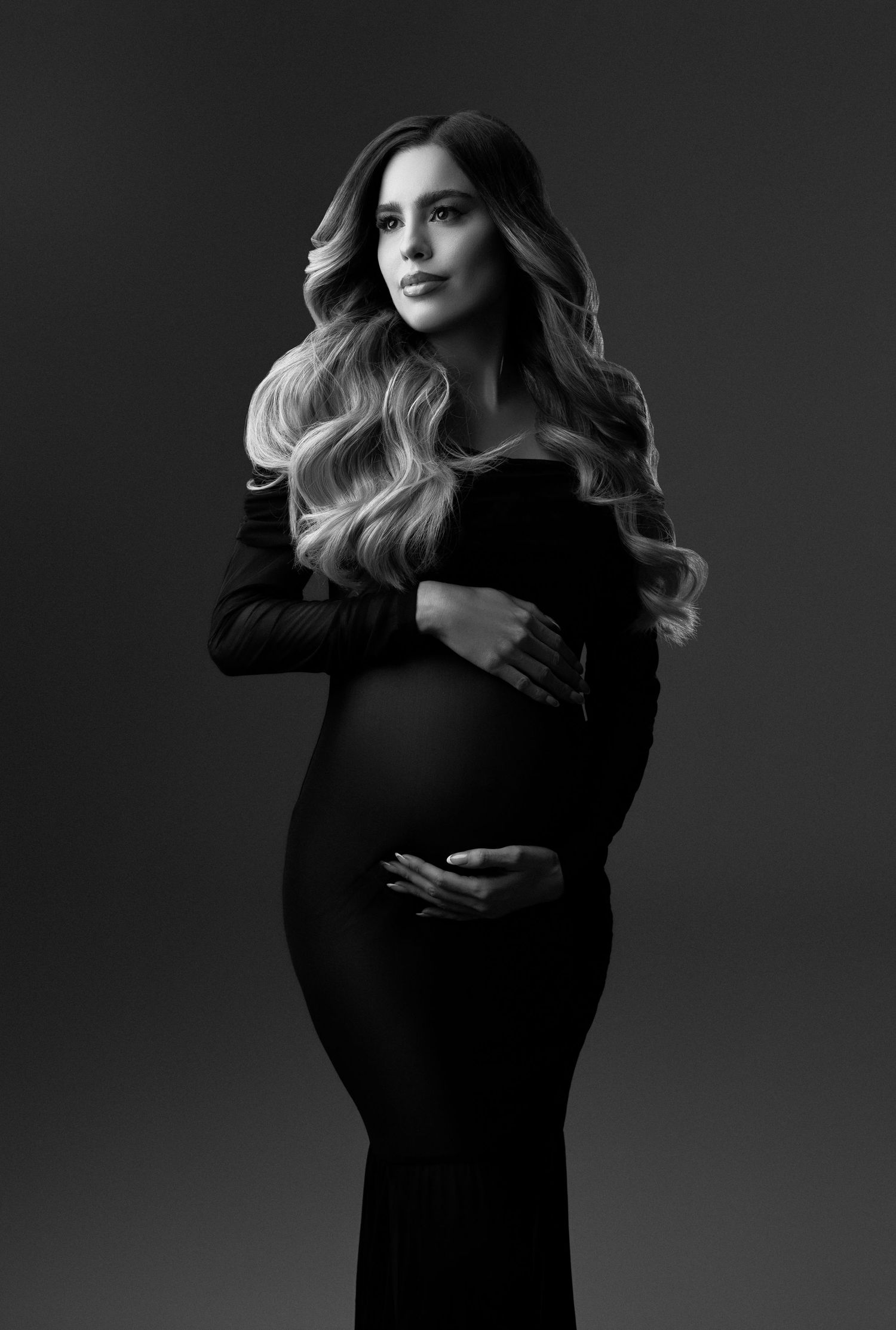 Woman with long wavy hair poses in a flowing champagne chiffon gown billowing dramatically against a dark studio backdrop.