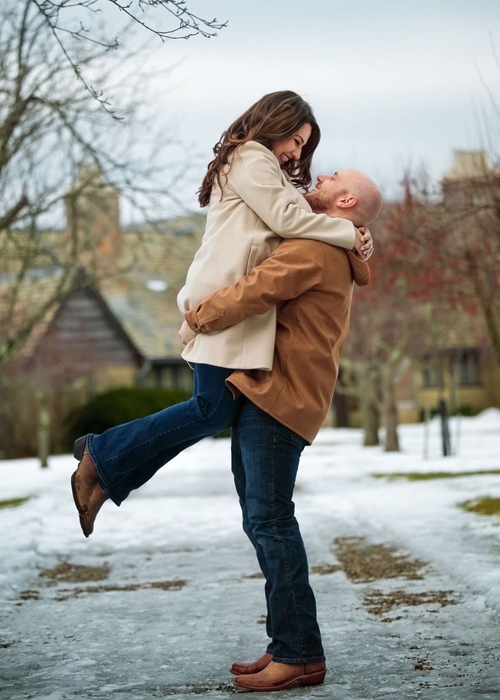 Man lifting woman in romantic embrace on snowy winter outdoor path.