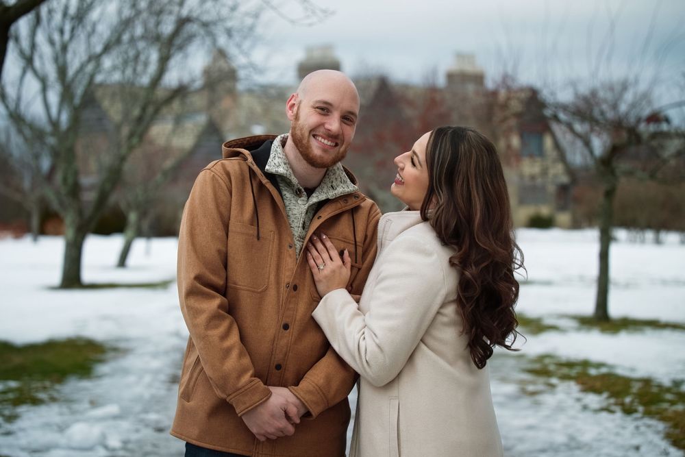 Smiling engaged couple embracing outdoors in winter snowy park setting.