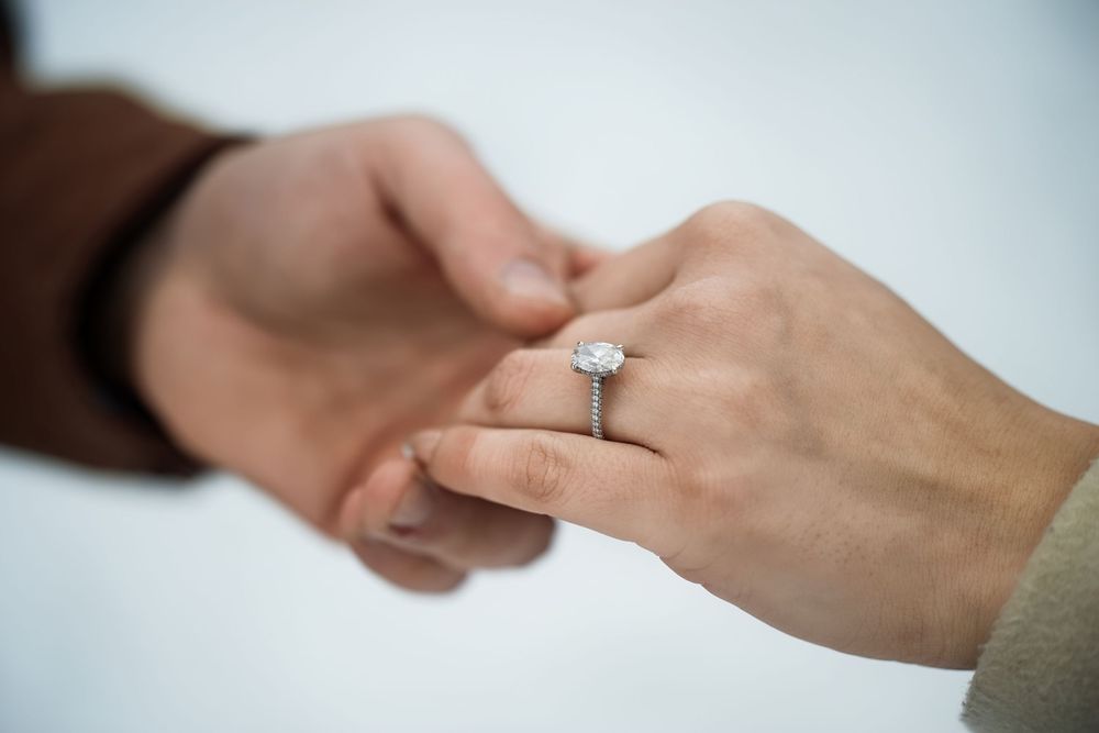 Close-up of diamond engagement ring on womans hand held by partner.