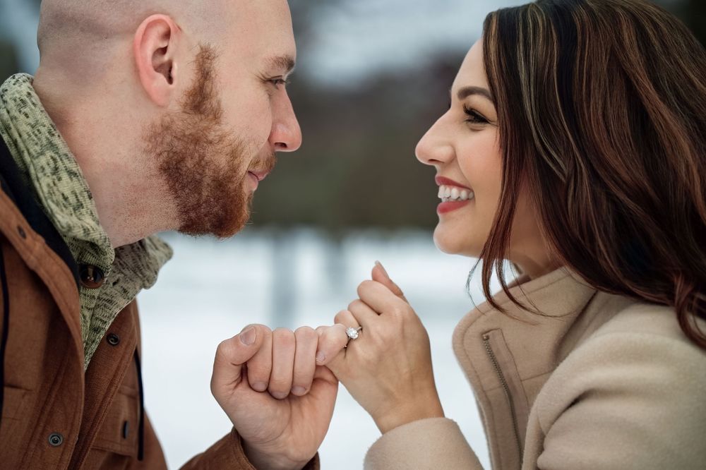 Couple holding hands and gazing at each other lovingly in a snowy winter outdoor setting.