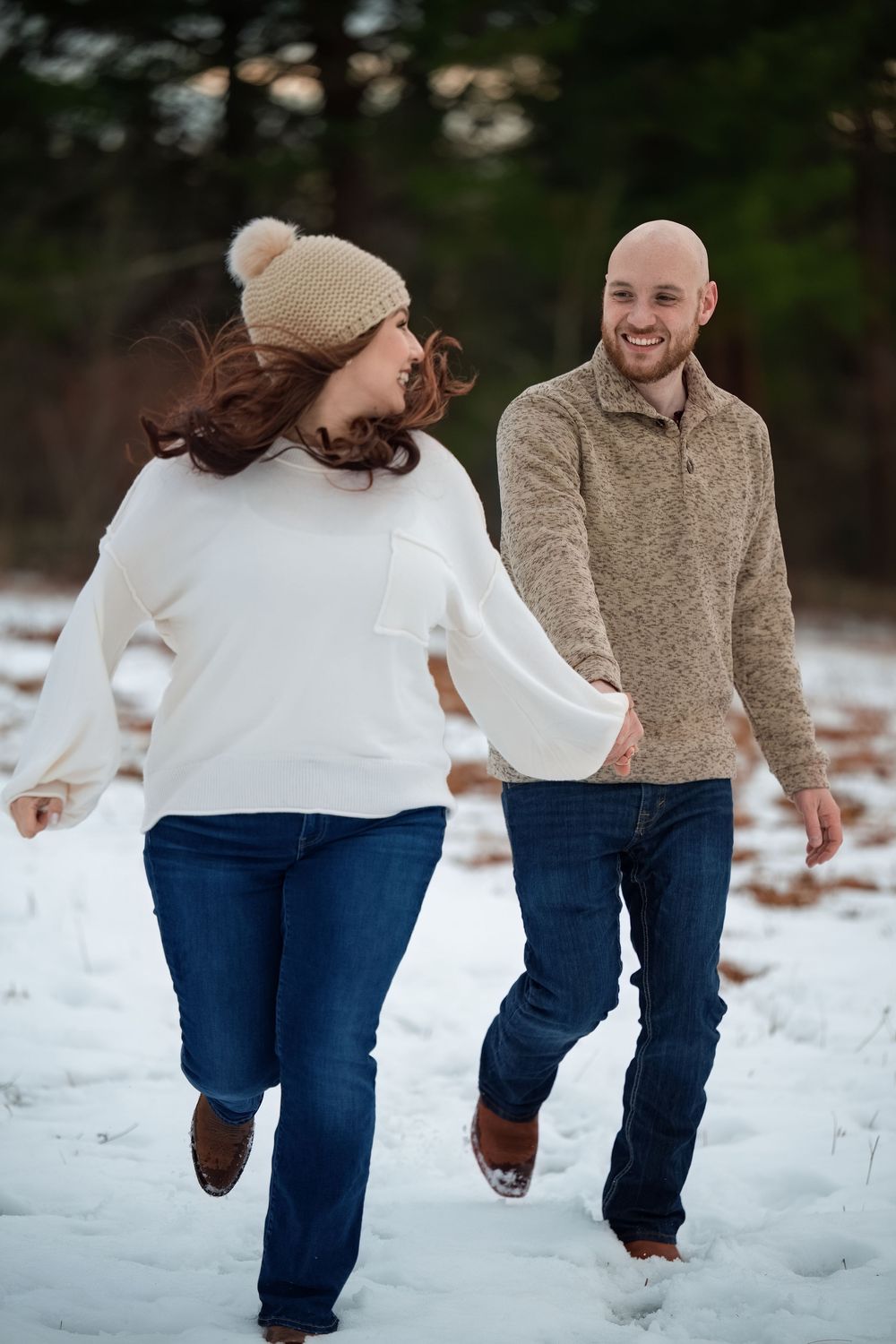 Happy couple holding hands and walking playfully through a snowy winter landscape.