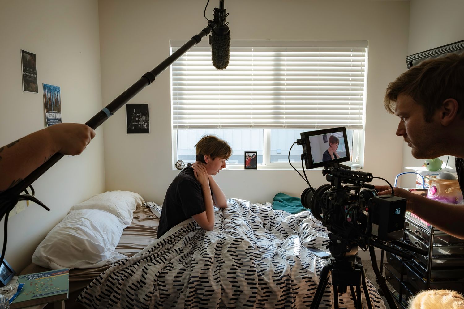 Film production setup in bedroom with cameras and crew visible through window light.