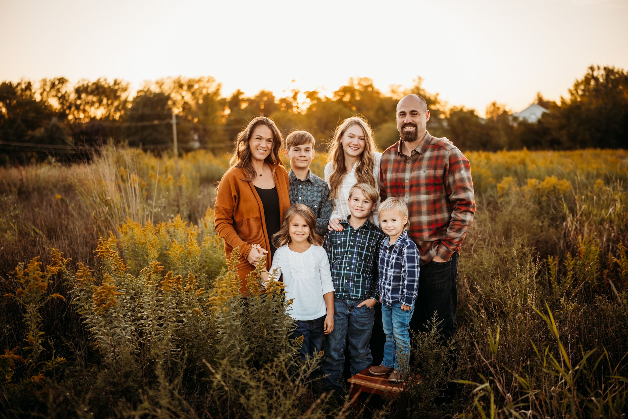 A group poses together in a golden field at sunset wearing casual fall clothing and plaid shirts.