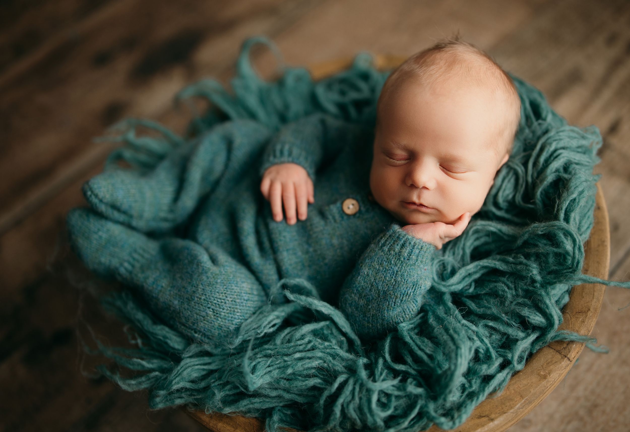Newborn baby wrapped in teal textured blanket sleeping peacefully during professional photo session.