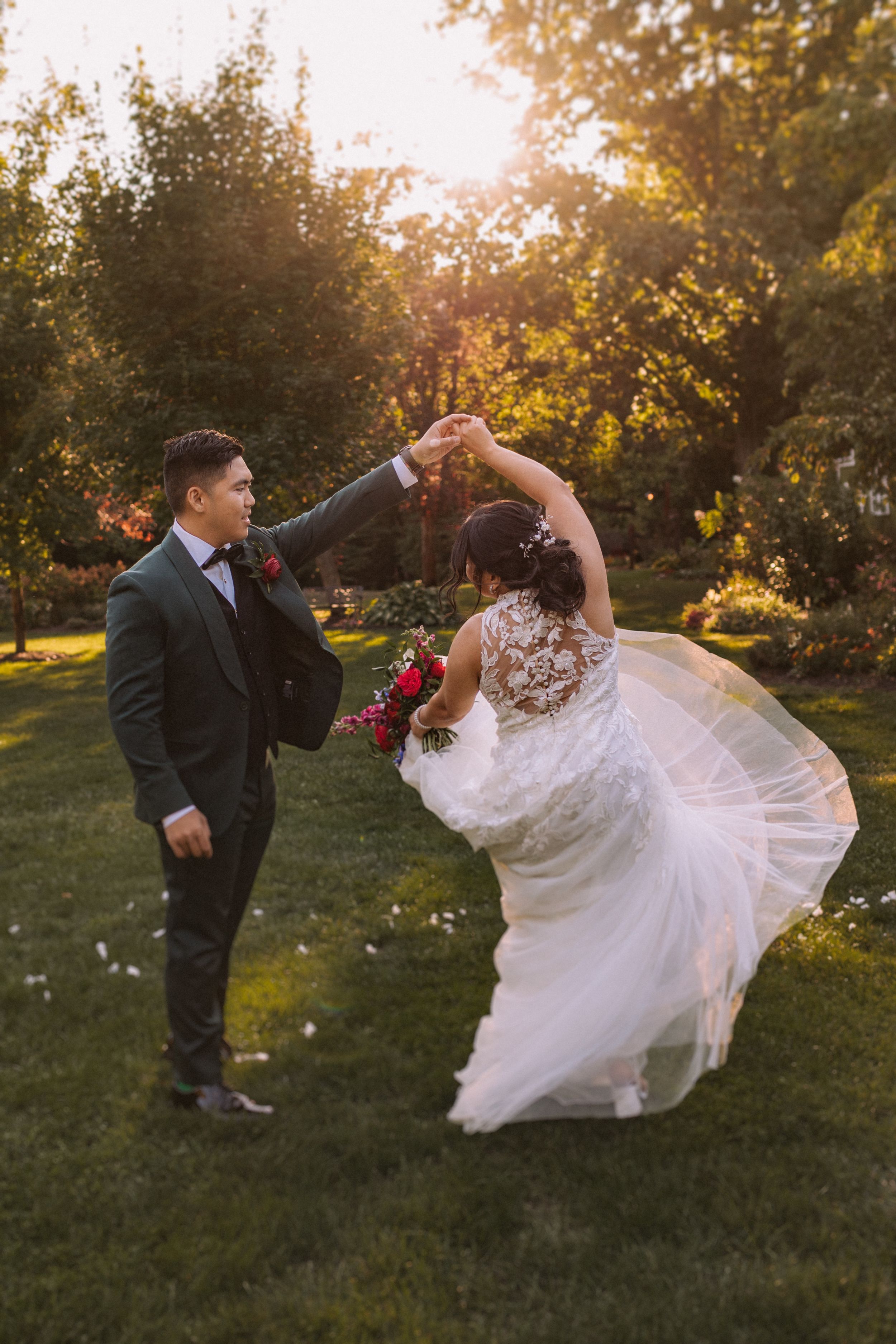 A couple dances together in a garden at sunset, with the bride's white dress flowing gracefully through the movement.