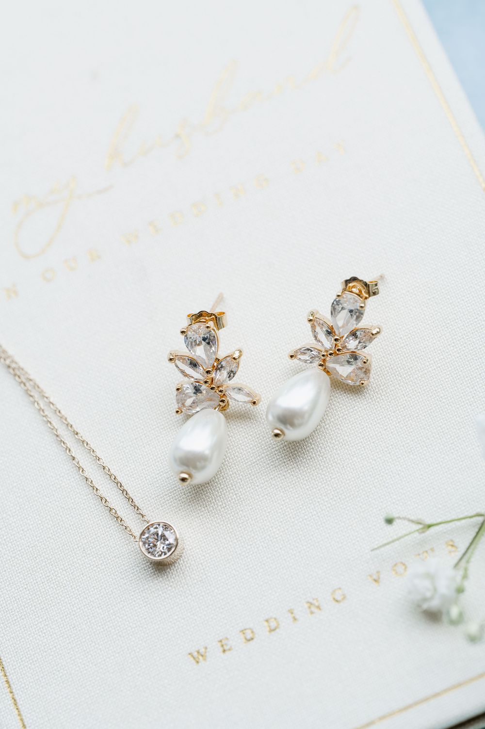 Pearl and crystal bridal earrings with delicate floral design on white wedding stationery.