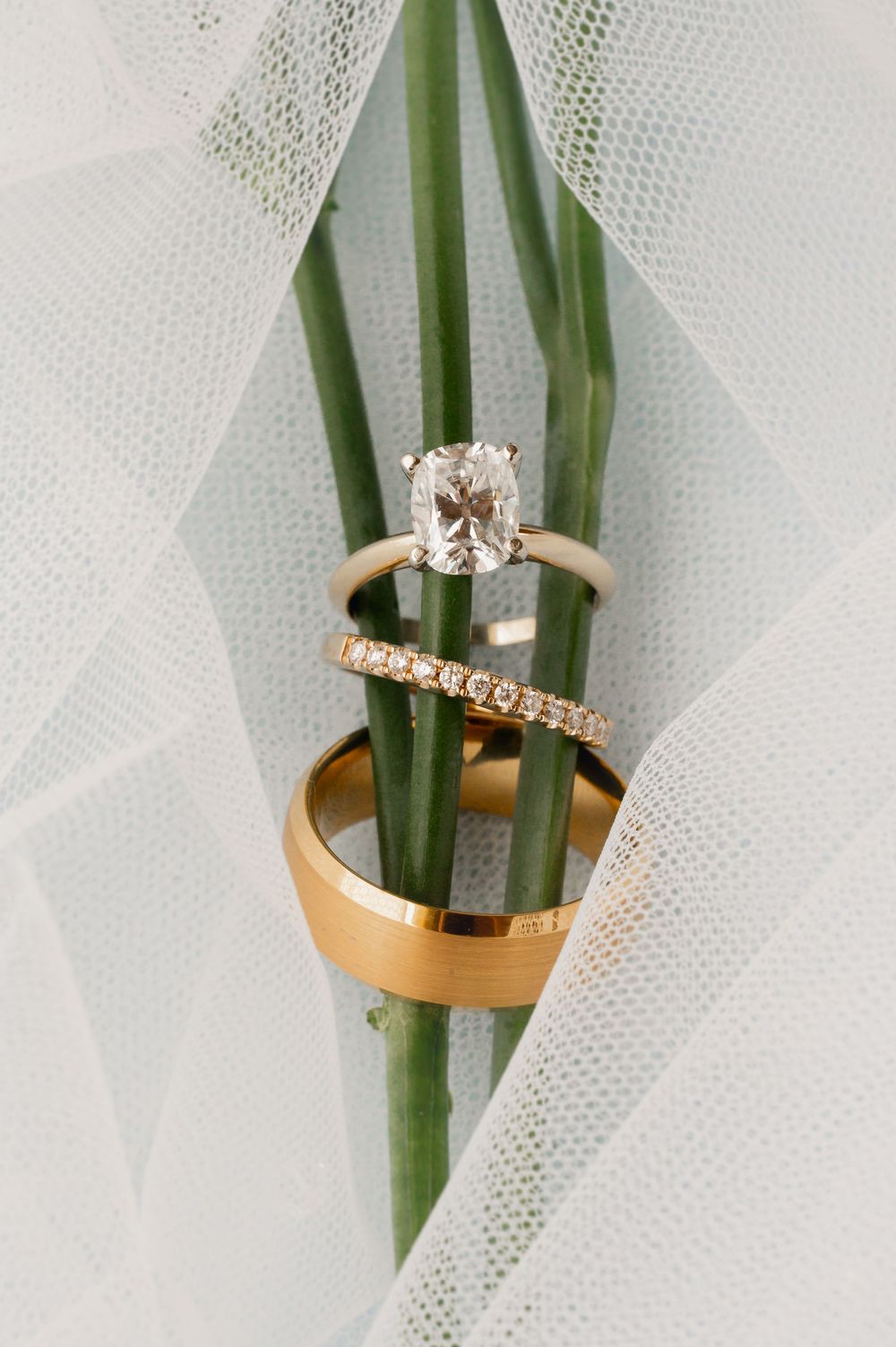 Wedding rings and diamond engagement ring styled with white tulle and green stems.