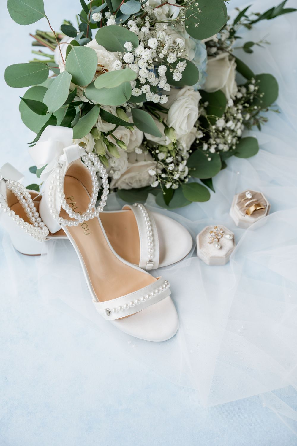 White bridal shoes with pearl details alongside eucalyptus and white floral bouquet.