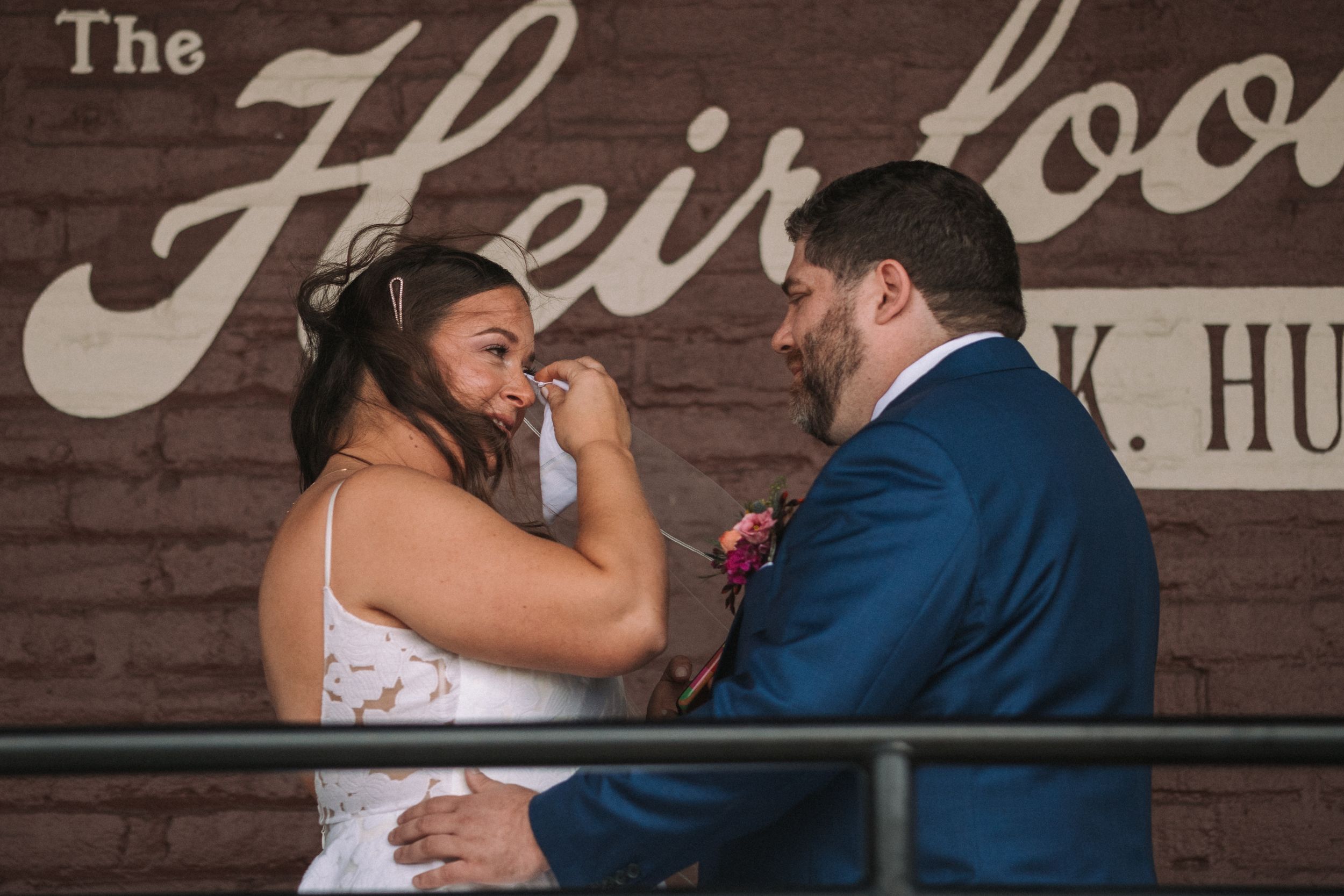 A couple shares an emotional moment at their wedding ceremony in front of a rustic wooden wall with vintage lettering.