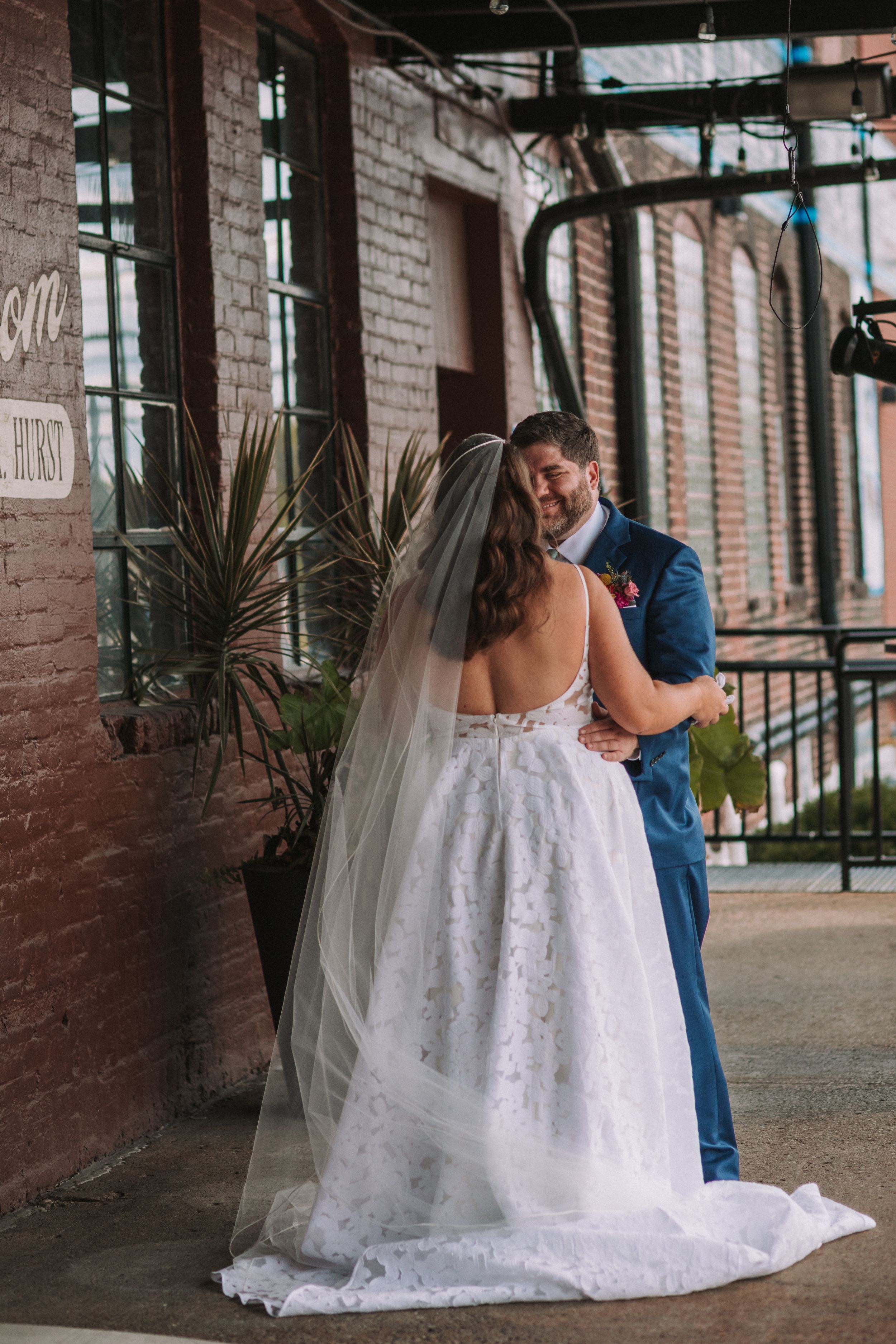 A couple shares an intimate moment on their wedding day, with the bride wearing a lace gown with flowing veil.
