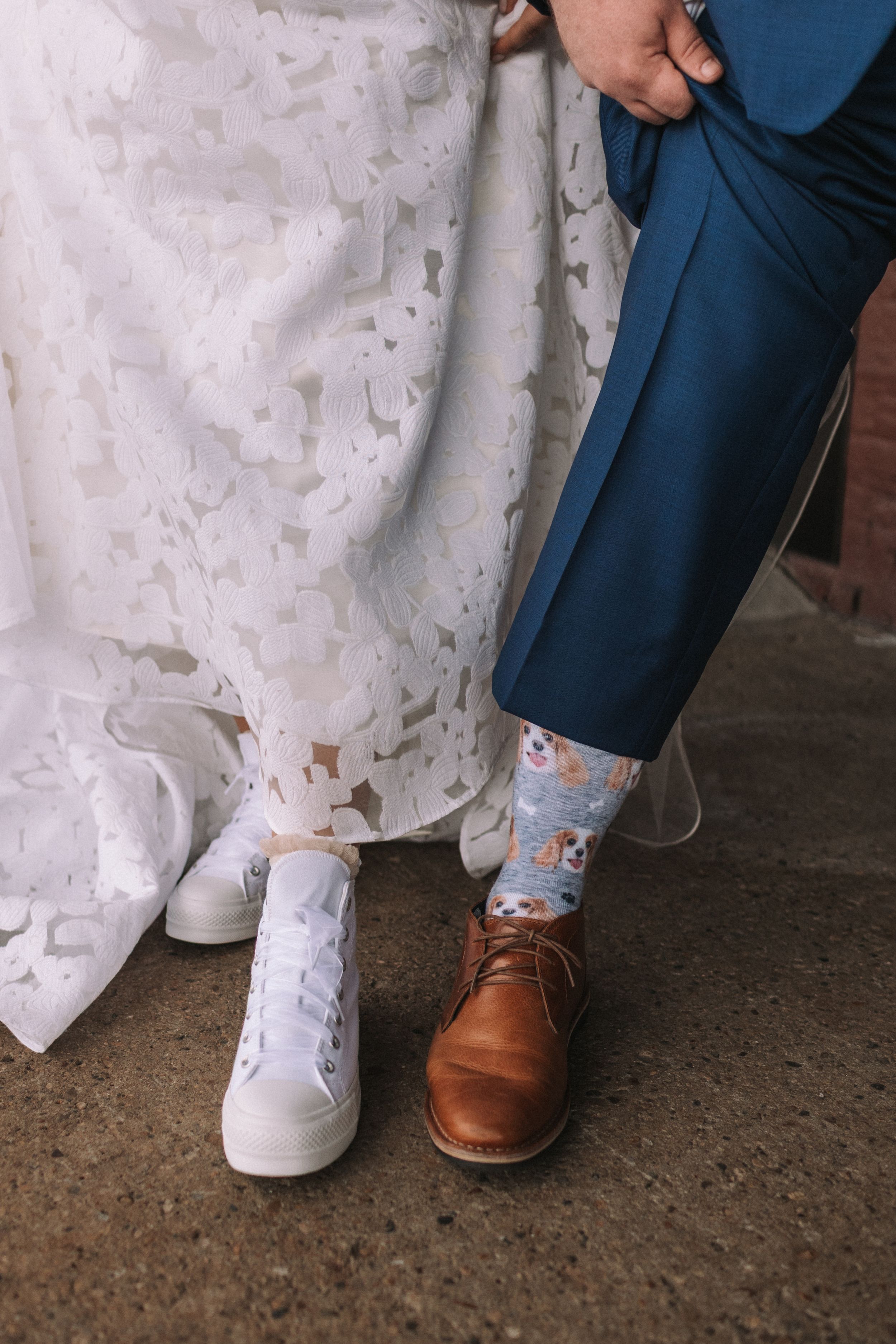 Close-up view of contrasting wedding footwear showing white sneakers and brown leather dress shoes with floral socks.