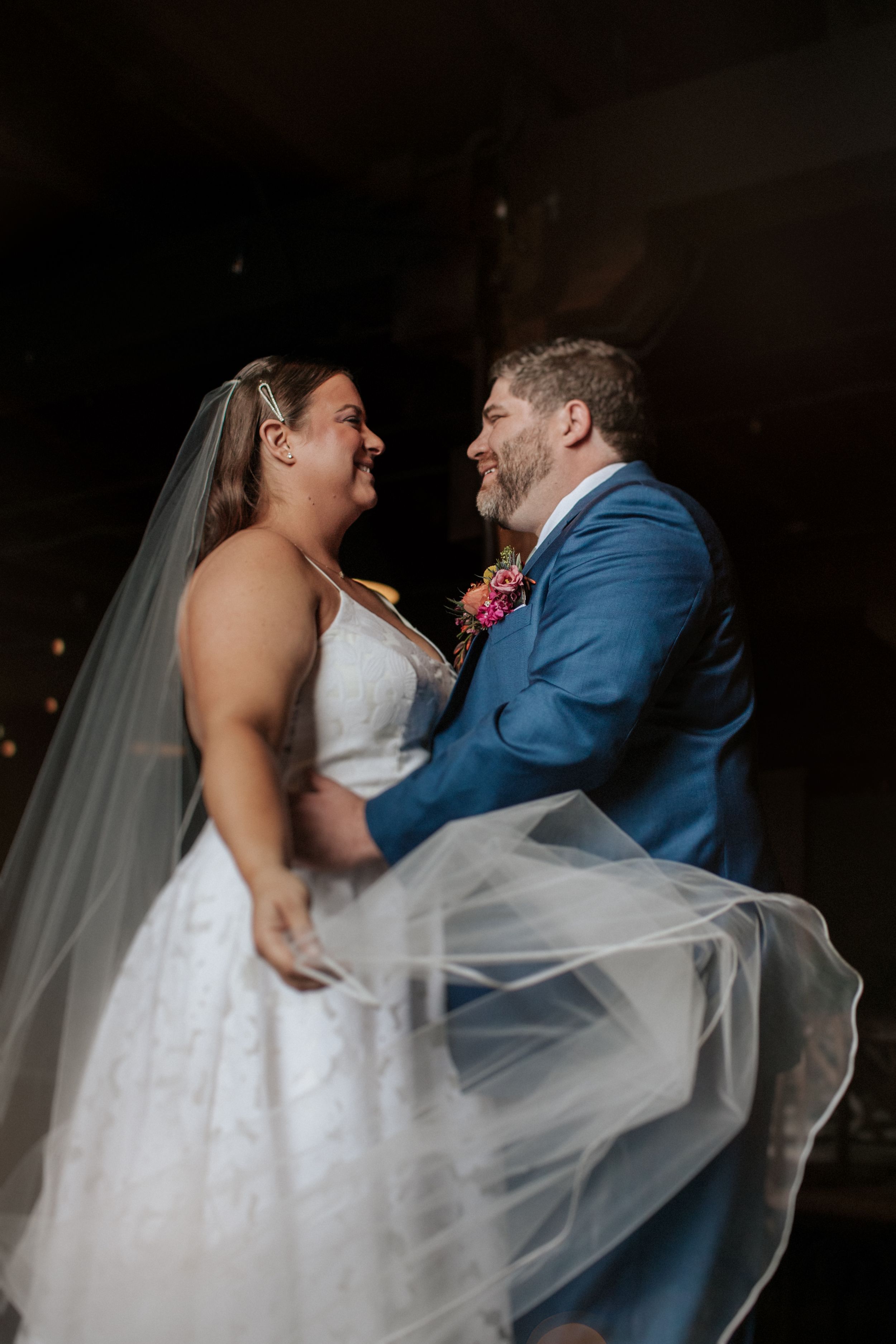 A couple in wedding attire dances together, with the bride's white dress and veil flowing elegantly as they move.