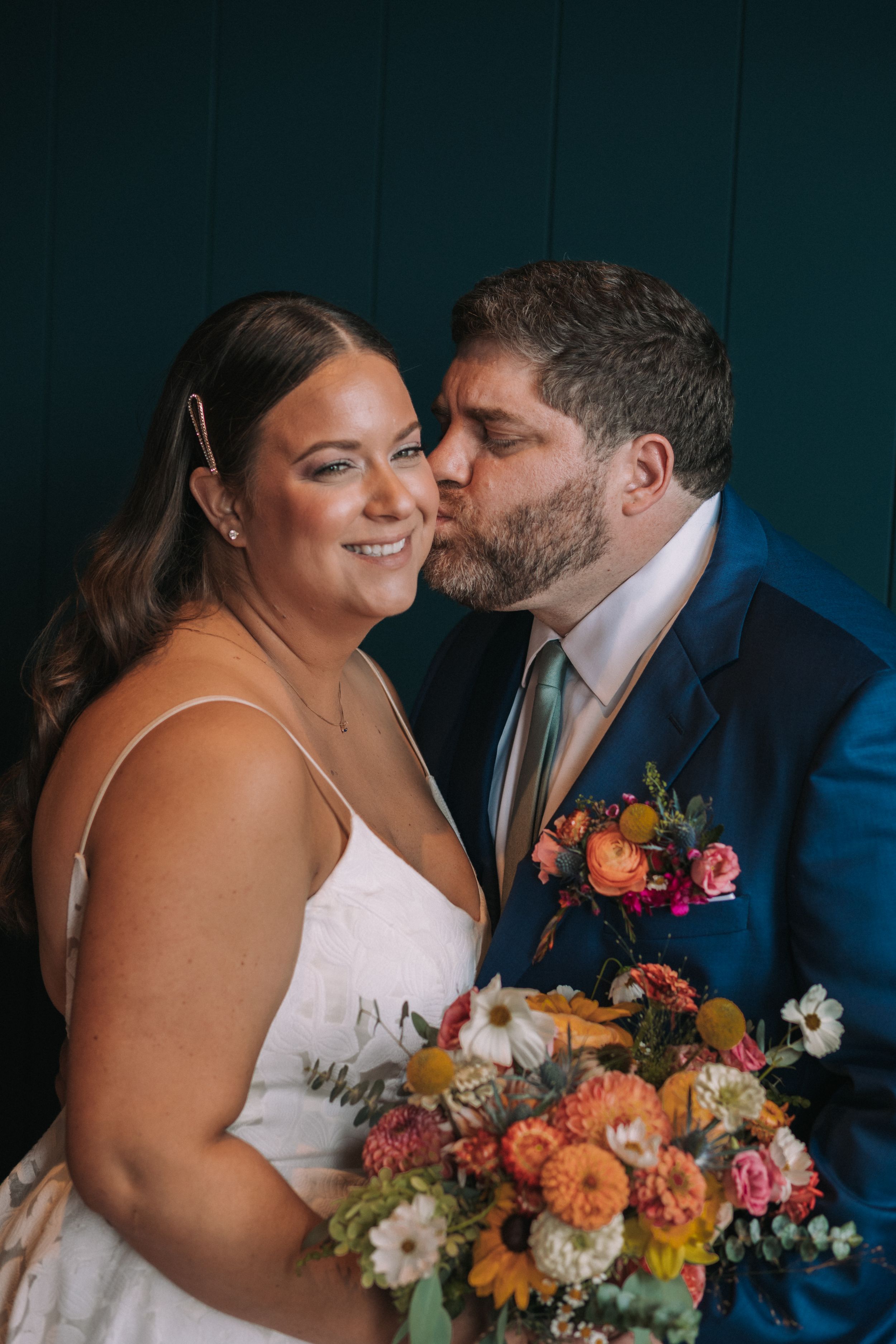 A couple shares an intimate moment with vibrant orange and pink florals at their wedding celebration.