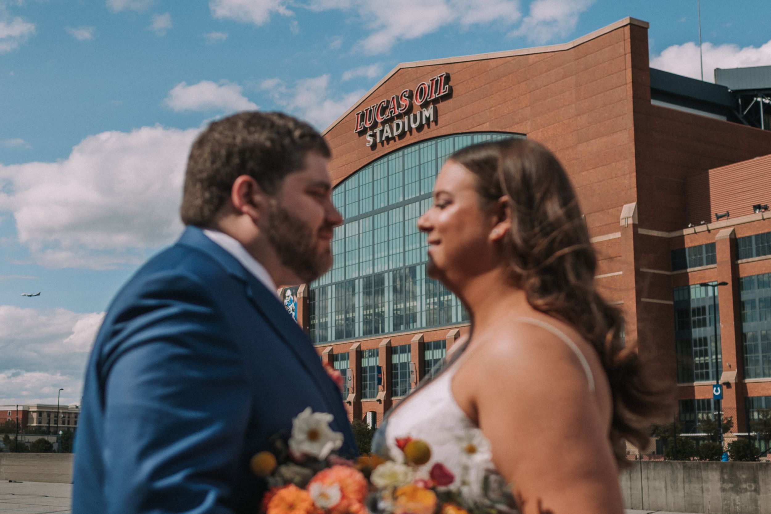 Wedding couple shares tender moments outside a modern brick building on a sunny day.