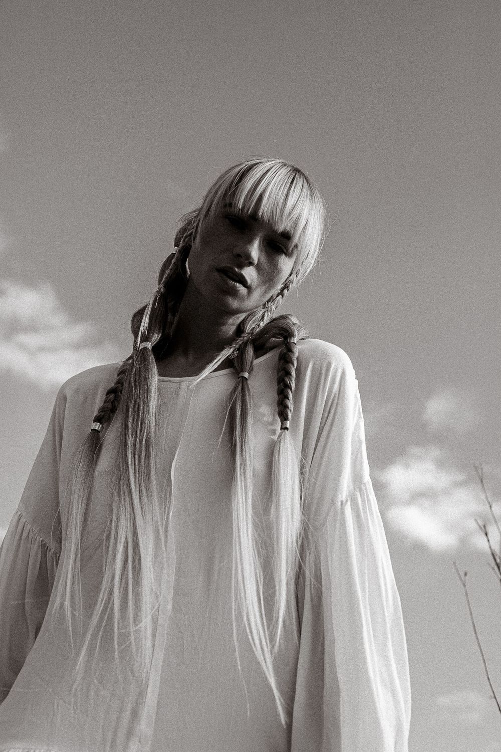 A series of black and white artistic portraits showing a figure with long blonde braids wearing white against a cloudy sky.