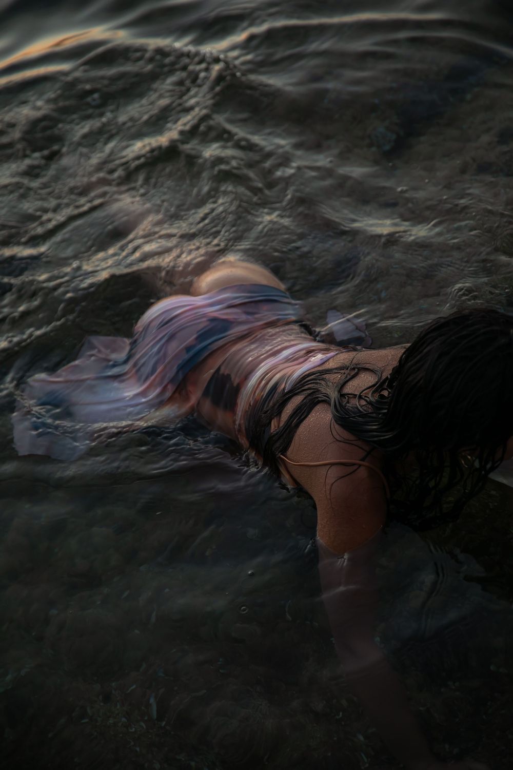 Dark moody photograph of long hair floating in rippling water during sunset creating ethereal patterns.