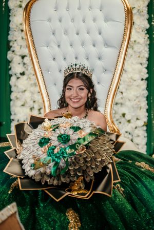 An elegant white tufted throne chair with gold frame surrounded by floral decorations.