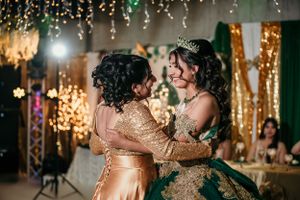 Two people embrace while dancing, one wearing a sparkly gold dress and another in an emerald ball gown.