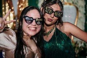 Two friends wearing party glasses pose together at a festive celebration.