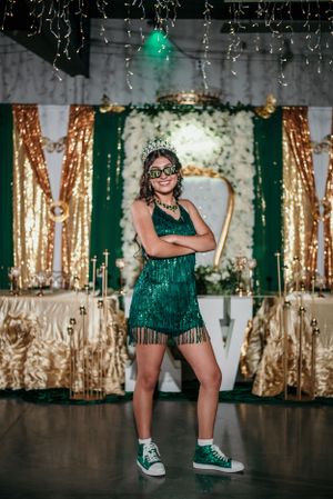 Person in green sequin dress and green sneakers poses confidently against gold and green backdrop.