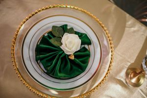 Elegant place setting features white rose on emerald green fabric with gold-rimmed plates.