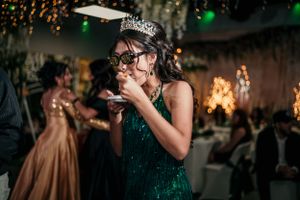 A celebration guest in an emerald green dress and tiara enjoys food at an elegant event.