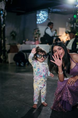 A child in colorful pajamas dances at a party while a woman in a purple dress poses nearby.