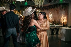 Two people dance together at an event, one wearing an emerald green dress and another in a champagne-colored gown.